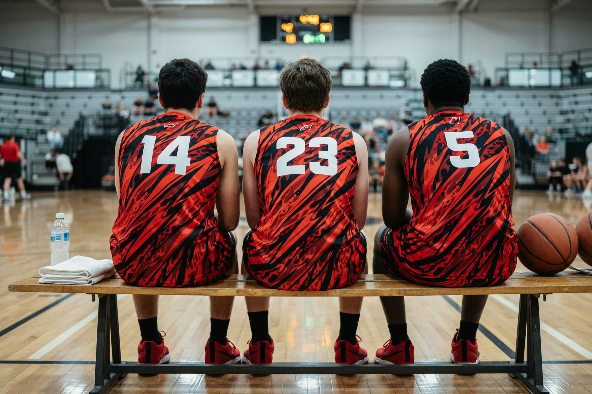Basketball players on the bench seen from behind in custom red and black flame jerseys with numbers 14, 23 and 5