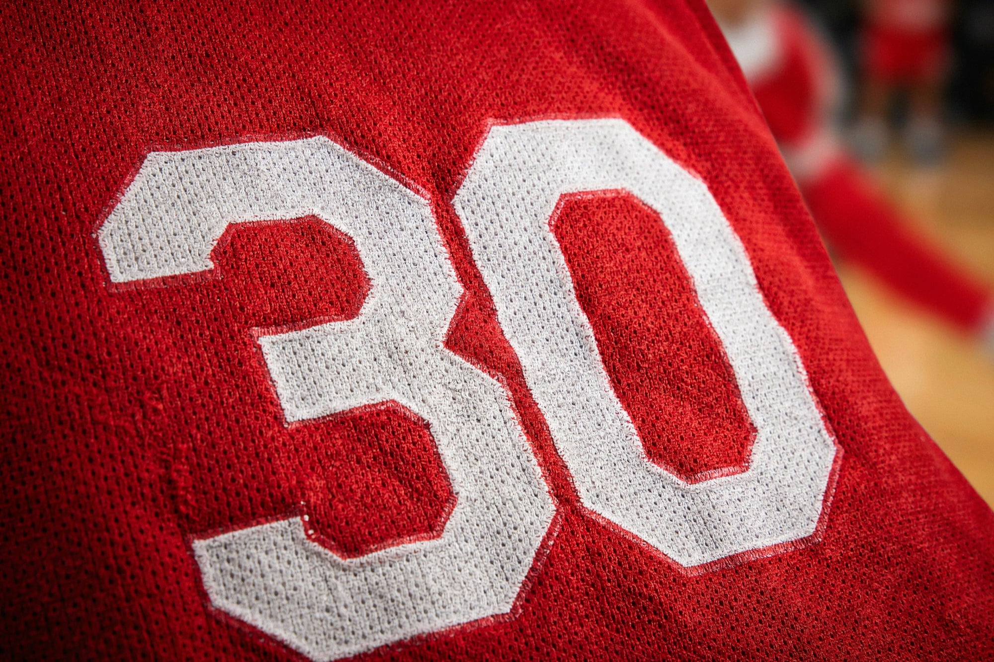 Close-up of red and white sublimated basketball mesh with the edge of a white number 30
