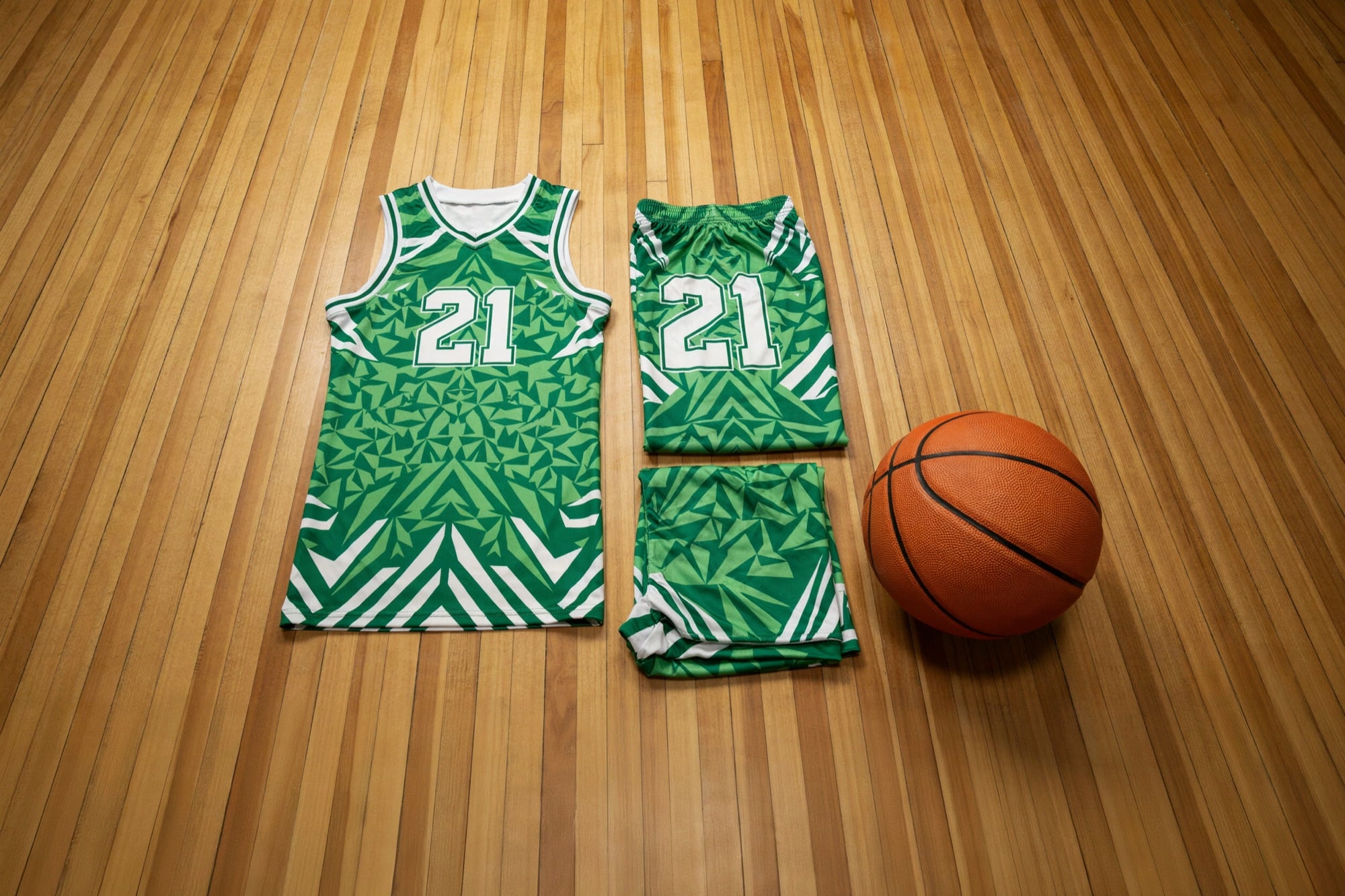 A custom green and white basketball jersey and shorts laid out on a gym floor beside a basketball