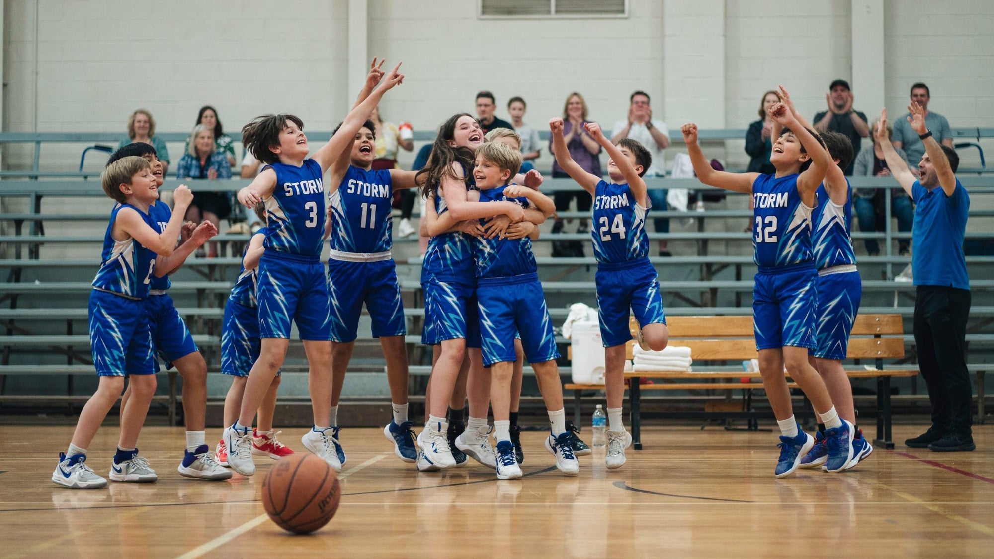 A youth basketball team celebrating together on a gym court in custom royal blue and white STORM uniforms