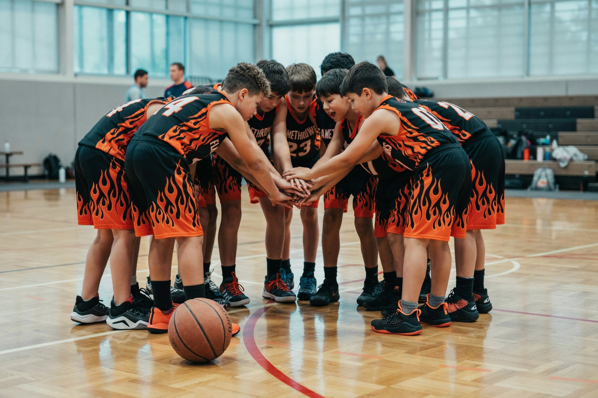 A youth basketball team huddling in custom black and orange flame uniforms
